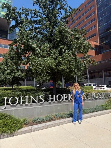Lene Bleich in blauer medizinischer Kleidung steht vor dem Schild des Johns Hopkins Hospital.